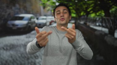 Genç adam, şehir sokaklarında park halindeki arabaların arasında özür dilemeden orta parmak hareketi yaparken gülüyor..