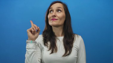 Beyaz gömlekli, pembe rujlu, mavi arka planda yukarıya bakan kadın düşünceli bir ifade sergiliyor. Fikir ve kavramlar aktarıyor..