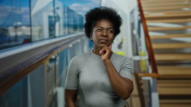 Teknedeki kadın düşünceli bir jest yapıyor, bir fikri işaret ediyor, deniz kenarındaki bir ortam ile çevrili, açık hava ortamlarıyla karakterize edilmiş ve sakin bir deneyim sunuyor..