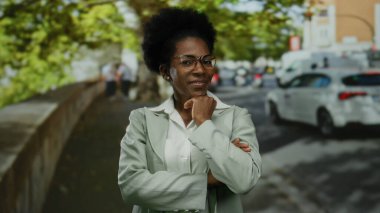 Şehir caddesinde arabaları ve ağaçlarıyla güvenle gülümseyen, gözlüklü ve gri takım elbiseli bir kadın, Afro-Amerikan açık hava dünyasının şehir yaşam tarzını gözler önüne seriyor..