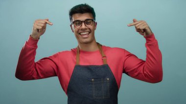 Gözlüklü ve önlüklü bir adam izole edilmiş mavi arkaplanı işaret ediyor..