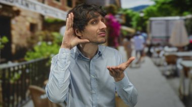 Lokanta terasında öne doğru eğilen açık mavi gömlekli genç adam kulağı masanın yanında, merak..