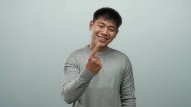 Gri süveter giyen genç Çinli adam izole edilmiş beyaz arka planda elleriyle jestler yapıyor, pozitiflikle gülümsüyor..