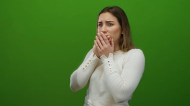 Yeşil arka planda şaşırmış bir kadın, izole edilmiş ortamı vurgulayan boş bir duvarla şok ve duygu tasvir ediyor..