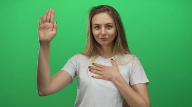 Yeşil izole edilmiş bir arka plana karşı duran beyaz gömlekli bir kadının el kaldırışı samimiyet duygusu ve doğruluk sözü yaratıyor..
