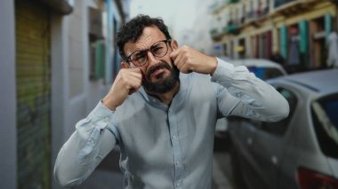 Sakallı İspanyol bir adam üzgün görünüyor ve arka planda arabalarla ve binalarla dolu bir sokakta ağlıyor..