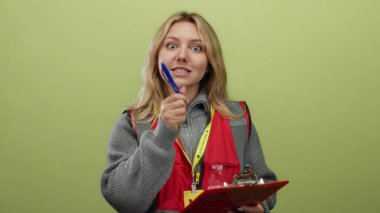 Genç gönüllü bir kadın elinde bir kalem tutuyor ve bir panoya, izole edilmiş mavi bir arkaplan duvarına yazıyor..