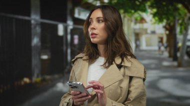 Şehir caddesinde akıllı telefon kullanan, odaklanmış ve meşgul bir kadın..