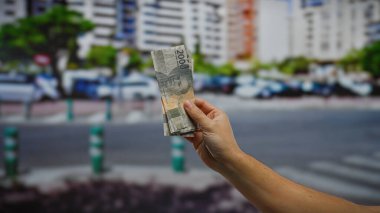 Endonezya rupiasını elinde tutan adam kentsel caddenin hareketli şehir ortamında finansal işlemleri yansıtıyor.