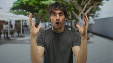 Restoran ortamında yapraklı tepe örtüsü altında ağzı açık ve elleri havada bir adam..