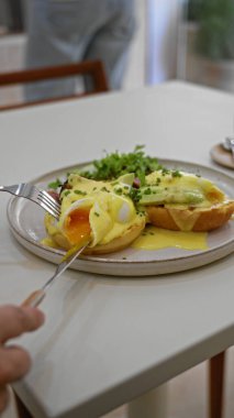 Lezzetli yumurtaların tadını çıkaran kişi, sıcak bir restoranda, içinde taze malzemeler ve parlak gün ışığı bulunan beyaz bir masanın üzerinde çatal ve bıçakla birlikte avakado ile birlikte..