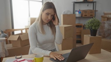 Yeni evde dizüstü bilgisayarla çalışan bir kadın. Oturma odasında doğal ışık ve modern iç tasarımı olan kutular ve bitkilerle çevrili..