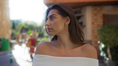 Şehir ortamında gezen bir kadın, şehir zeminine karşı güzellik ve gençlik gösterisi yapan doğal ışıklandırma özelliklerini ön plana çıkaran, sıcak ve canlı bir atmosferi işaret eden bir kadın..