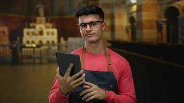 Gözlüklü genç adam kilisenin içinde tablet tutuyordu. Süslü mimari ve kemerlerle, günlük önlükler giyiyordu. Kapalı alanda yansıtıcı bir şekilde dikilirken kendine güvenini gösteriyordu..