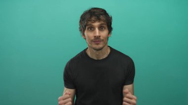 Yumruklarını sıkmış ve gülümseyen genç bir adam stüdyo duvarının önünde kutlama yapıyor..