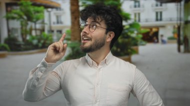 Sakallı, yeşil ve bulanık şehir geçmişi olan bir sokakta gülümseyen genç bir İspanyol..