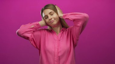 Pembe gömlekli genç bir kadın kulaklarını elleriyle kapatıyor, pembe bir arka plana karşı hayal kırıklığını ifade ediyor, izolasyon ve duygusal stres hissi veriyor..