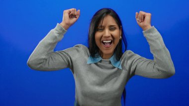 Neşeli mavi arka planda kutlama yapan bir kadın, neşeli bir ifadeyle mutluluk ve başarıyı ifade ediyor..