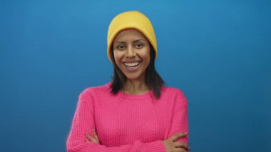 Genç İspanyol kadın, parlak sarı beresi ve pembe süveteriyle mavi bir arka planda gülümsüyor.