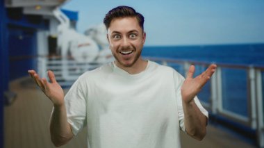 Gemi güvertesinde sırıtan sakallı genç bir adam açık havada güneşli bir günde deniz zeminine gülümsüyor..