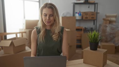 Yeni apartman dairesinde çalışan bir kadın oturma odasında dizüstü bilgisayar kullanarak yeşil ve ışık dekoru elementleriyle hareket ettiğini gösteriyor..