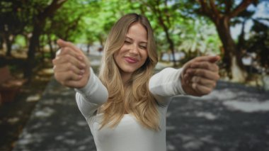 Gözleri kapalı sarışın bir kadın ve yeşil parkta nazik bir gülümseme ile omuzlarına sarılıyor..