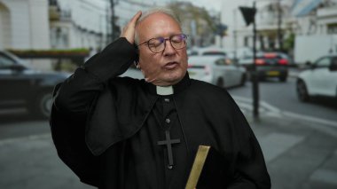 Başrahip, arka planda araçlar ve binalar olduğunu belirtirken elinde bir kitap tutuyor..