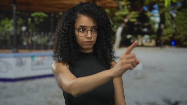 Siyah bir üst parmak takan genç İspanyol kadın yeşilliğin ortasında bir caddede nesneyi işaret ediyor..