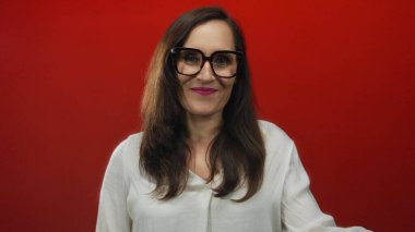 Uzun koyu renk saçları ve beyaz gömleğiyle canlı kırmızı bir arka plana gülümseyen bir kadın genç İspanyol bir kadının modern ve kendinden emin bir portresini oluşturuyor..