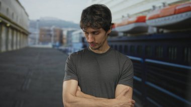 Genç adam kollarını kavuşturup sanayi caddesinde demirlemiş bir teknenin yanında başını eğiyor. Reddedilmiş..