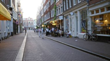 Güneşli bir günde Amsterdam 'da kafelerin ve dükkanların önünden geçen insanların şehir yaşamını canlı mimari ve sosyal toplantılarla gösteren bulanık sokak manzarası.