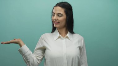 Genç İspanyol kadın gülümsüyor ve elini mavi bir duvara doğru uzatıyor, özgüven ve duruş ile sunum ya da tanıtım öneriyor.
