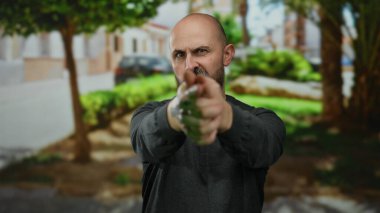 Kel sakallı adam şakacı bir şekilde şehir sokaklarında ağaçlarla ve şehir geçmişiyle parmak tabancası yapıyor..