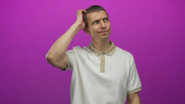 Kafkasyalı bir adam parlak pembe arka plana karşı kafa karışıklığı içinde yalnız başına düşünceli bir ifadeyle dikiliyor ve günlük beyaz gömlek giyiyor..