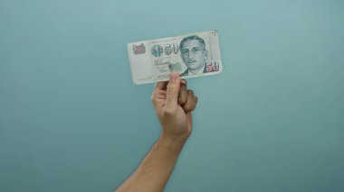 Tek bir banknot tutan bir adam mavi bir duvara karşı arka plan, basit bir ayar içinde finans ve para vurguluyor.