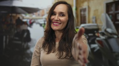 Sıcak bir restoranın terasında uzanmış gülümseyen bir kadın hareketli bir caddede hoş bir jesti canlı bir ortamda yakalıyor..
