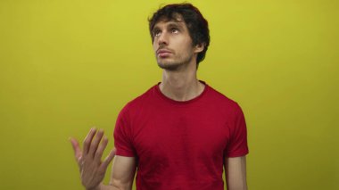 Kırmızı tişörtlü genç adam sarı stüdyo duvarına bakıyor; sakin iç gözlem odağı ve sakin.