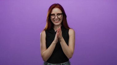 Mor arka planda mutlu bir şekilde alkışlayan bir kadın kırmızı saçlı, gözlüklü ve günlük kıyafetleriyle neşeli bir ifade sergiliyor, canlı basitlikte pozitif enerji ve zarafet sergiliyor..