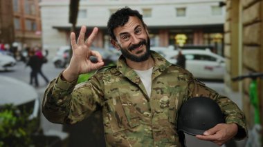 İspanyol üniformalı bir adam kalabalık bir sokakta elinde miğfer tutarak gülümsüyor. Bu da kendine güveni ve açık havada pozitif tutumunu gösteriyor..