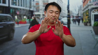 Kırmızı gömlekli genç adam arka planda binalar ve araçlarla kalabalık şehir sokaklarında hareketli bir şehir atmosferini taşıyor..