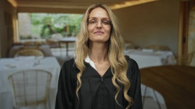 Avuç içi işaret eden bir kadın restoranda durmuş siyah üniforma giyen genç sarışın bir yargıç gibi gülümsüyor..