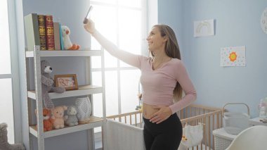 Bebek odasında beşik ve doldurulmuş hayvanlarla gülümseyen annelik ve modern iç mekan tarzında mutluluğu gösteren selfie çeken bir kadın..