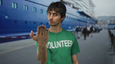 Gönüllü genç adam doğrudan liman terminalini gösteren kameraya işaret ediyor; kamu hizmeti sürücü nişanı.