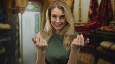 Kapalı bir yerde, rahat bir dükkan ortamında renkli halılarla çevrili bir şekilde gülümseyen bir kadın, neşeli, çekici bir tavır sergiliyor..