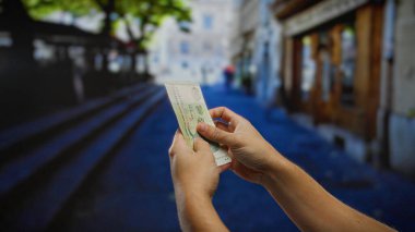 Canlı bir şehir caddesinde tek başına dolar sayan adam, bulanık şehir geçmişiyle odaklanmış elleri gösteriyor, seyahatin hem finansal hem de kültürel yönlerini vurguluyor..