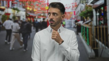 Beyaz gömlekli genç İspanyol adam kırmızı fenerlerle kaplı kalabalık bir caddede parmak dudağa hareket ediyor; sessizlik..