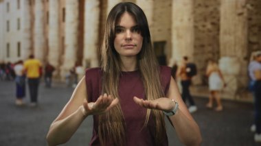Şehir sokaklarında sakinlik için el kol hareketi yapan, bulanık kalabalığın ve tarihi mimarinin ortasında İspanyol genç bir kadını gösteren bir kadın..