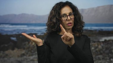 Orta yaşlı İspanyol kadın parmak ucuyla Sandy Rocky Sahili 'ni işaret ediyor..