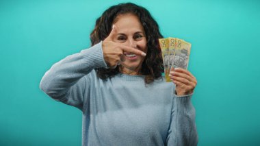 Avustralya banknotları tutan kadın mavi duvara gülümsüyor, canlı bir ortamda para gösteriyor, finansal başarı ve pozitiflik öneriyor..