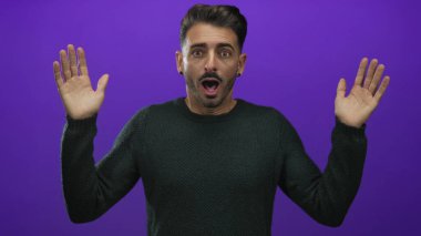 Stüdyoda ağzı açık bir adam elini kaldırıyor, avuçlar öne bakıyor canlı mor alana karşı; sürpriz şok.